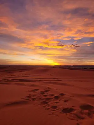 a sunset on the beach with footprints in the sand at Amrad luxury camp in Merzouga
