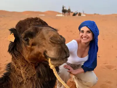 a woman standing next to a camel in the desert at Merzouga Experience Camp in Merzouga