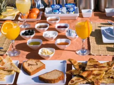 a table with plates of food and glasses of orange juice at Merzouga Experience Camp in Merzouga