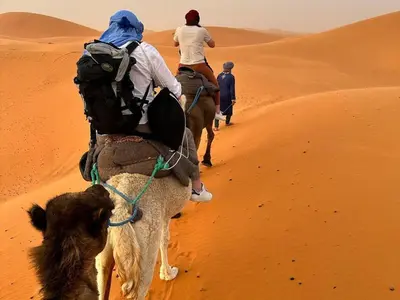 two people riding on the back of a camel in the desert at Merzouga Experience Camp in Merzouga