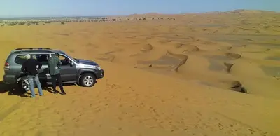 a group of people standing next to a car in the desert at Merzouga Erg Merzouga Camp in Merzouga