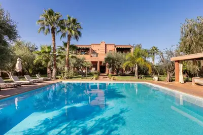 a swimming pool in front of a house with palm trees at Villa Layyine avec personnel, piscine, spa et sports in Marrakech