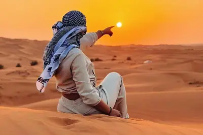 a man sitting in the desert pointing at the sun at Soul Dunes Luxury Camp in Merzouga