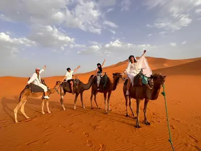four people riding on camels in the desert at Desert Nomads Camp in Merzouga