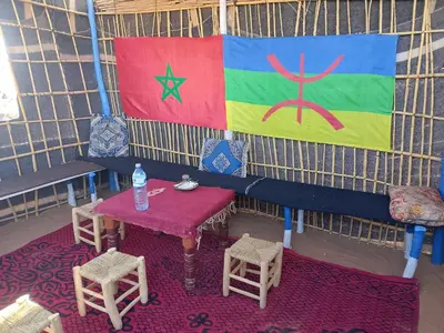 a tent with a table and chairs and a flag at Merzouga your Tour Nigths in Camp in Merzouga