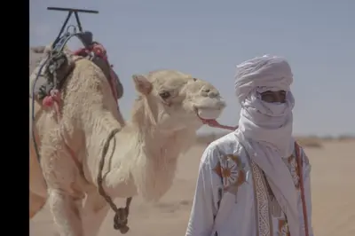 a man standing next to a camel in the desert at Sahara Escape tours in Mhamid