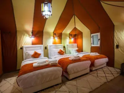 a bedroom with three beds with orange and white pillows at Diamond luxury camp in Merzouga