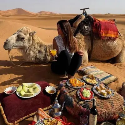 a woman sitting next to a camel in the desert at Merzouga Spectacular Luxury Camp in Merzouga