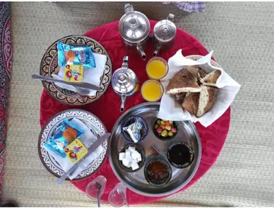 a red table topped with plates of food and bread at Hami desert camping in Merzouga