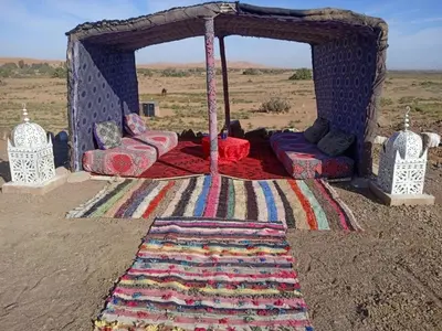 a bed in a tent in the desert with a rug at Hami desert camping in Merzouga