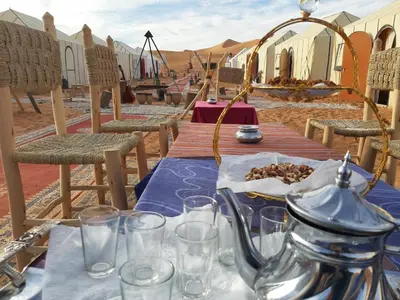 a table in the middle of a desert with a table with glasses at Merzouga campsite in Merzouga