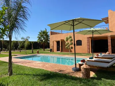 a house with a swimming pool with a umbrella and chairs at Dar Mazaheer in Ouanina