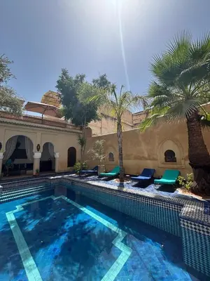 a large swimming pool with chairs and palm trees at Chambres Émeraude et Rubis - Riad Lotus Bleu in Fès