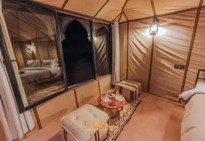 a room with a tent with a table and a bed at Desert Rose Camp in Merzouga