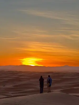 two people standing in the desert watching the sunset at Desert Rose Camp in Merzouga