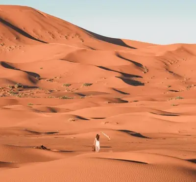 a person walking in the desert with a camel at Riad Dar Menorca in Merzouga