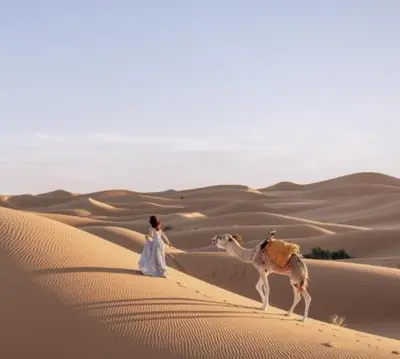 a woman and a camel in the desert at Riad Dar Menorca in Merzouga