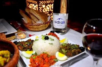 a plate of food with rice and a bottle of wine at discover luxury camp in Merzouga