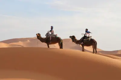 two people riding on camels in the desert at chez zakaria luxury tent camp merzouga in Erfoud