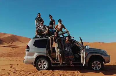 a group of people sitting on the roof of a vehicle in the desert at Merzouga Berber Luxury Camp in Merzouga