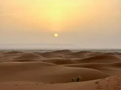 a sunset over a desert with the sun in the sky at Moroccco Desert Luxury Tents in Merzouga