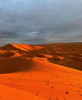 a desert with red sand and a cloudy sky at Moroccco Desert Luxury Tents in Merzouga