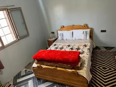 a bedroom with a wooden bed with red sheets and a window at Dar Taznakhte Entre Tapis et Traditions in Tazenakht