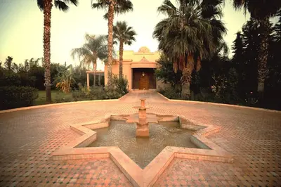 a fountain in front of a building with palm trees at Splendide Villa 5 chambres de luxe PRIVATISEE avec Cuisinière - Piscine chauffée - Jacuzzi & Hammam in Had Abdallah Rhiat