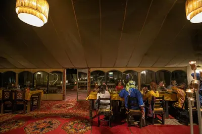 a group of people sitting at tables in a restaurant at Morocco Tours Camp in Merzouga