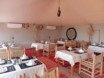 a dining room with tables and chairs in a tent at Kalimba Luxury Desert Camp in Merzouga
