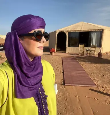 a woman wearing sunglasses and a purple hijab standing in front of a tent at Kalimba Luxury Desert Camp in Merzouga