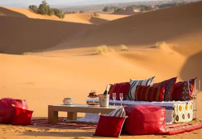 a table with red and blue pillows in the desert at Desert Camp in Merzouga