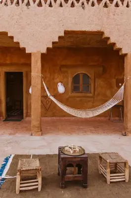 a patio with a hammock and tables in a building at Auberge Itrane merzouga in Merzane