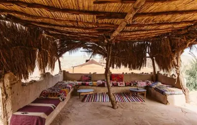 a group of couches sitting under a straw umbrella at Auberge Itrane merzouga in Merzane