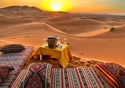 a table in the desert with the sunset in the background at Sahara Starlight Luxury Camp in Merzouga