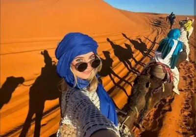 a woman in the desert with her camel caravan at Moroccan luxury camp in Merzouga