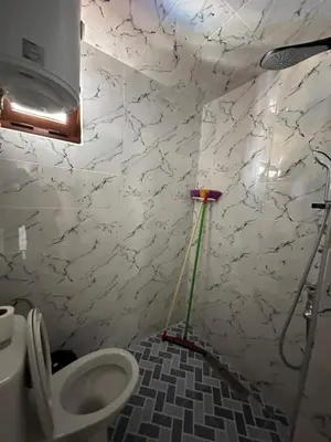 a bathroom with a toilet with a mop on the wall at Taghazout Hostel in Oulad Akkou