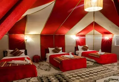 a room with three beds in a red and white tent at Desert Berber Luxury Camp in Merzouga