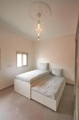 a white bedroom with two beds and a chandelier at Family Stay Ourzazate - Deluxe Appartments in Ouarzazate