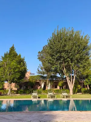 a swimming pool with two picnic tables and a tree at Domaine du souffle d Amaia in Had Abdallah Rhiat