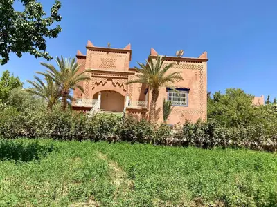 a large house with palm trees in front of it at Chez l'habitant tigminnagh in Ouarzazate