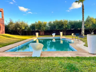 a swimming pool with two white chairs in the grass at Villa Zeen Garden in Marrakech