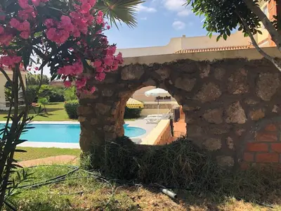 a stone wall next to a swimming pool with flowers at Beautiful villa with large private pool in Zaouia Sidi Rahkal