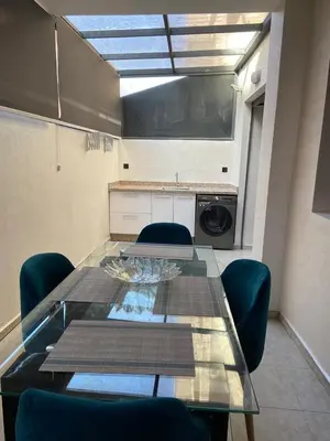 a dining room table with blue chairs and a kitchen at Duplex in Oulad Akkou