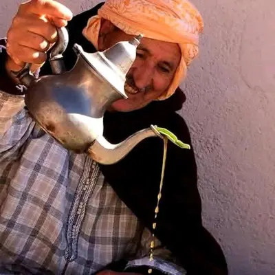 a man wearing an orange turban drinking from a tea kettle at Gite Likemte Tachdirt in Tacheddirt