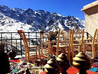 a table and chairs in front of a snow covered mountain at Gite Likemte Tachdirt in Tacheddirt