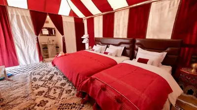a bedroom with two beds with red and white sheets at Nada luxury desert camp in Merzouga