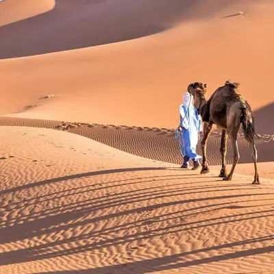 a man walking a camel through the desert at Nada luxury desert camp in Merzouga