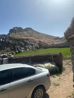 a car parked next to a stone wall and a hill at Anmid Tigmi in Tagdourt