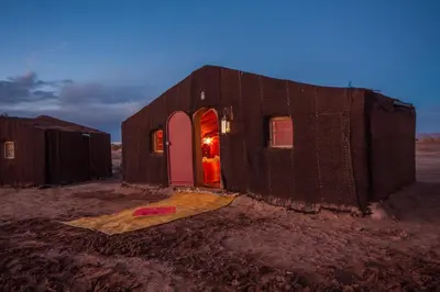 a small house with a pink door in the desert at Sahara Desert Camp Mhamid - Bivouac Le Pacha in Mhamid